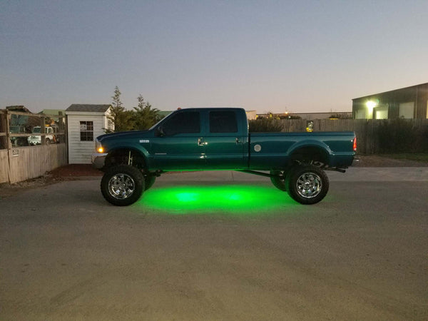 Black Oak LED rock lights glowing green under a vehicle, the rock lighting this article covers.
