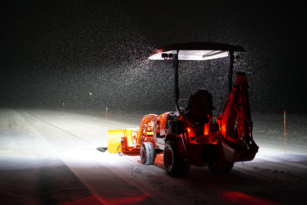 A tractor plowing snow after dark under bright LED work lighting, agricultural equipment working after dark on LED lighting.